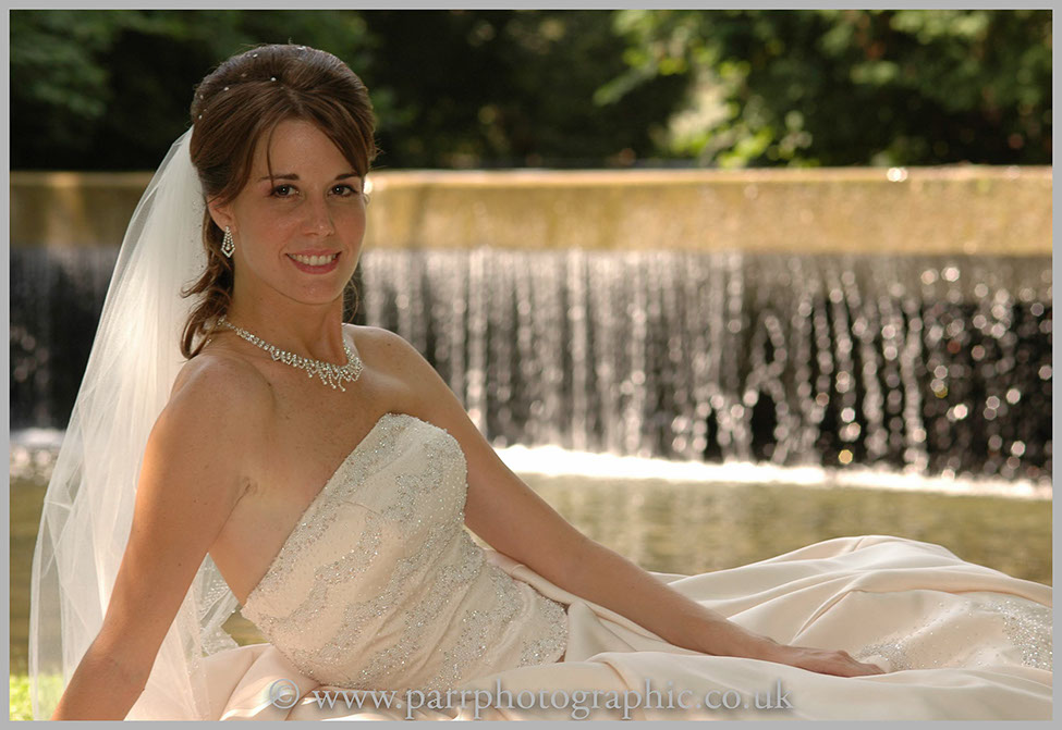 Bride sits on the grass in front of a waterfall
