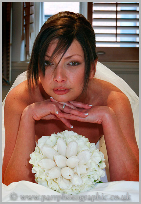 Bride lies on a bed with her bouquet of flowers under her arms